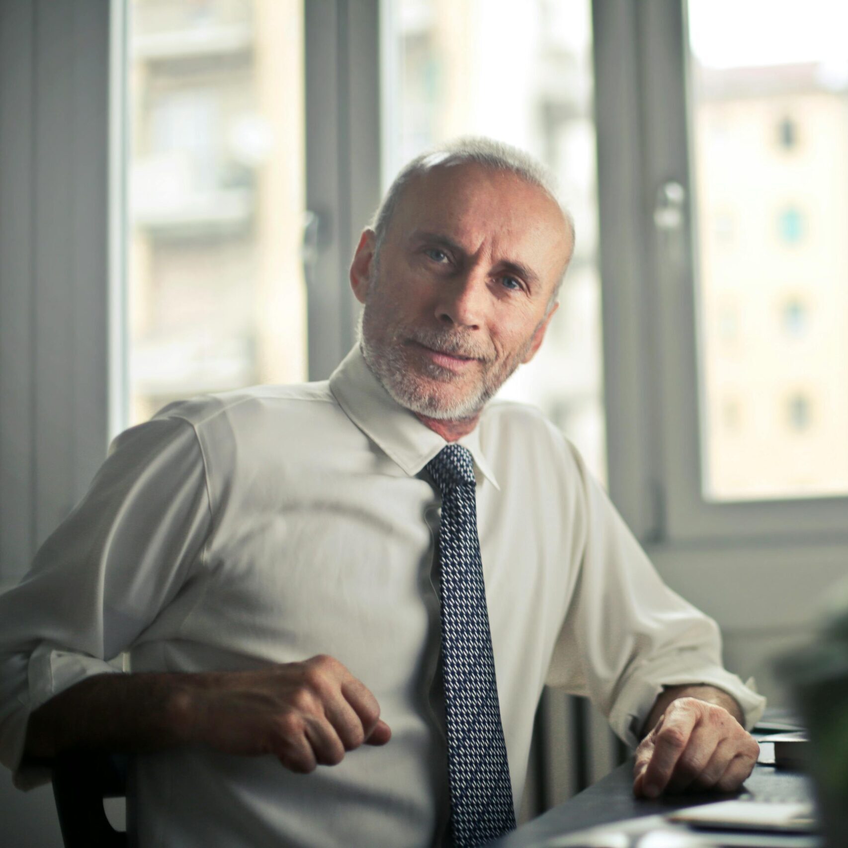 A mature man in professional attire smiling in an office setting.