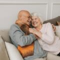 Happy elderly couple embraced in a cozy home setting, sharing joyful smiles.