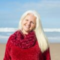 Senior woman in red sweater smiling at the beach in Portugal, a perfect blend of happiness and scenic ocean view.